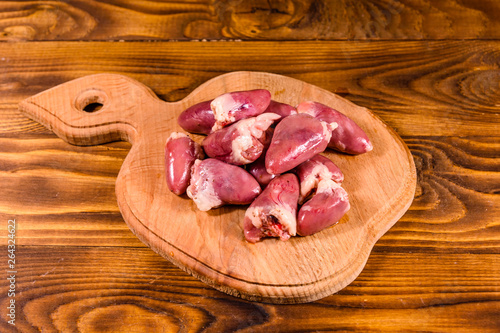 Cutting board with raw chicken hearts on wooden table