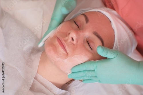 The girl goes through facial treatments in the beauty salon. Beautician wearing gloves apply moisturizer on the woman's face. Facials at the Spa