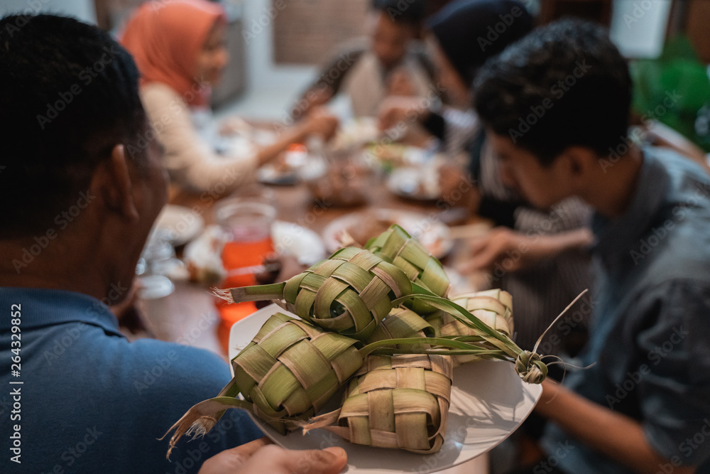 close up of ketupat with people eating dinner on the background. focus on ketupat or rice cake. eid mubarak celebration fasting