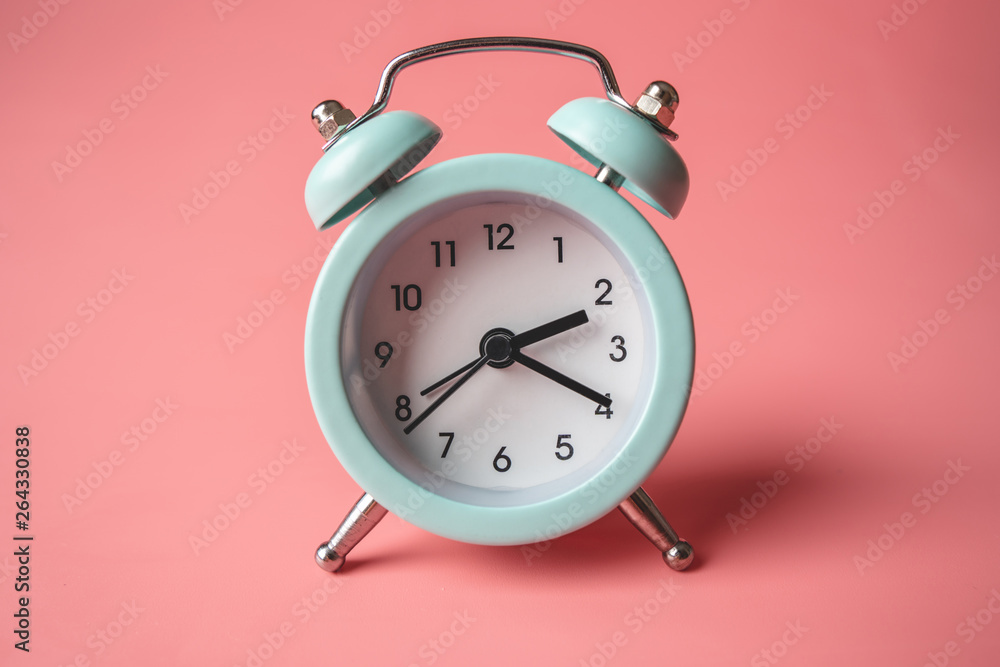 Blue analog metal alarm clock on stylish pink background. Concept of time in pastel colors Blue analog metal alarm clock on stylish pink background. Concept of time in pastel colors