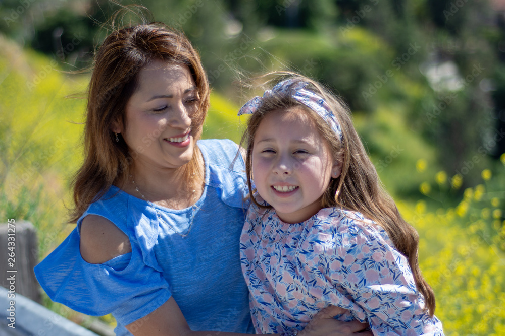 Latina Mother and Daughter Smiling and laughing on a hill in front of yellow flowers Latina Mother and Daughter Smiling and laughing on a hill in front of yellow flowers