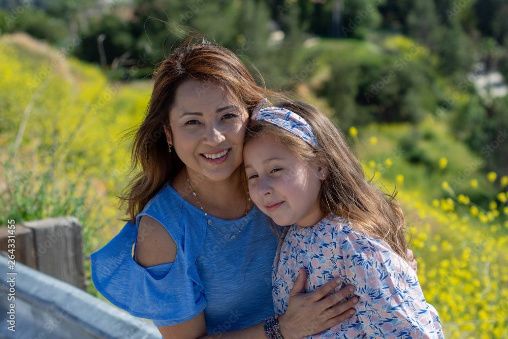 Latina Mother and Daughter Smiling and laughing on a hill in front of yellow flowers Latina Mother and Daughter Smiling and laughing on a hill in front of yellow flowers