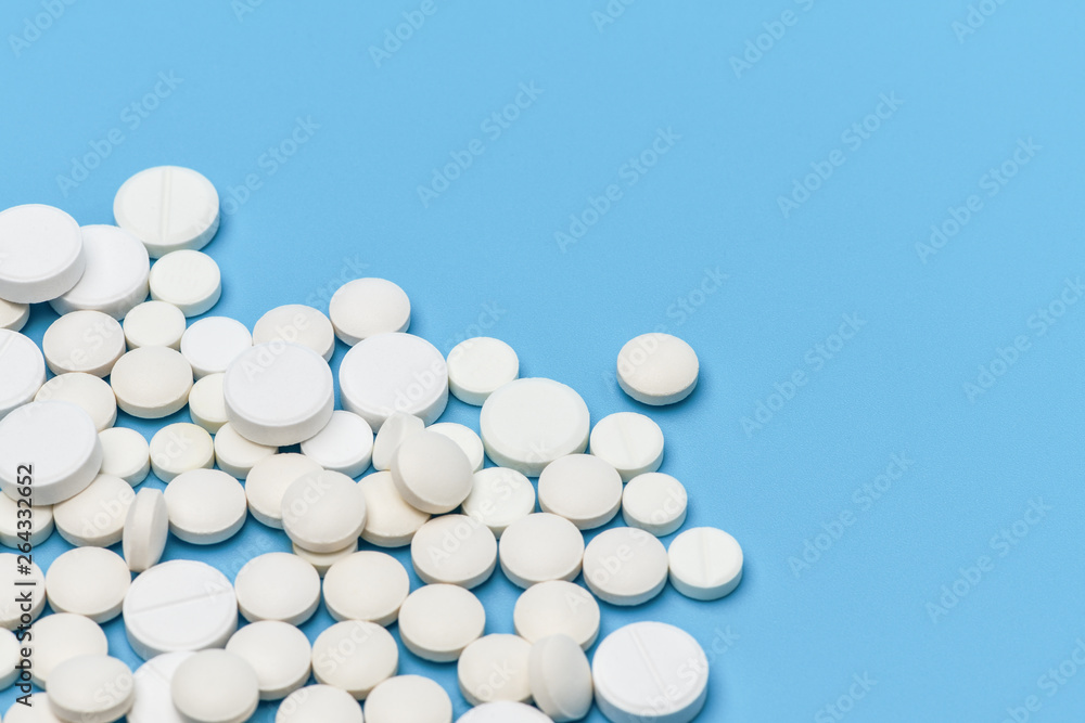 Lots of round white pills on blue background. Medication scattered on a blue background. Medical background. Health, Pharmacy, healthy lifestyle. Copy space for advertisement Lots of round white pills on blue background. Medication scattered on a blue background. Medical background. Health, Pharmacy, healthy lifestyle. Copy space for advertisement