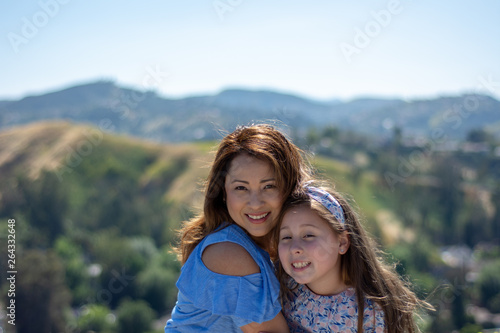 Latina Mother and Daughter Smiling and laughing on a hill in front of yellow flowers
