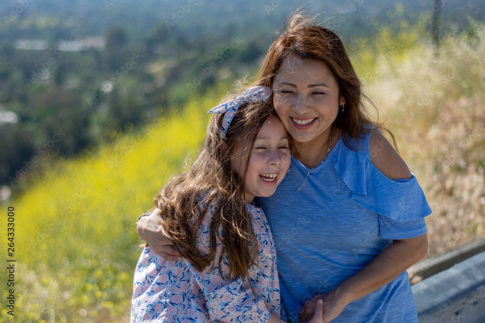 Fototapeta premium Latina Mother and Daughter Smiling and laughing on a hill in front of yellow flowers