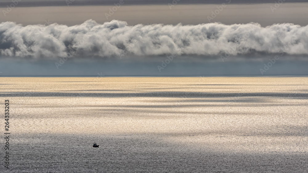 Obraz premium A wide view of the Irish Sea off the coast of Wales with silver glittering water and a small fishing boat on the sea.