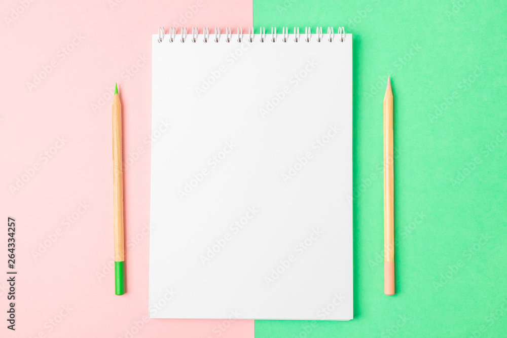 White open notebook on green and pink backgrounds. Nearby are pencils. Bright concept, flat lay, minimalism. Top view, copy space. White open notebook on green and pink backgrounds. Nearby are pencils. Bright concept, flat lay, minimalism. Top view, copy space.