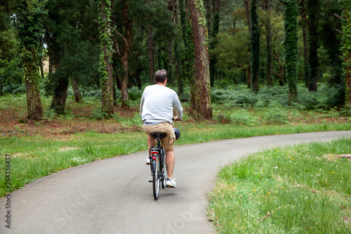 Man riding a bicycle in the summer park. Cyclist in beige shorts. Cycle path. View from the back. Active lifestyle