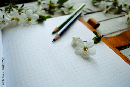 On the table is an open notebook, around a notepad of a branch with flowers of cherry
