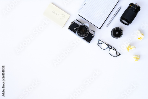 Creative flat lay photo of plain white desk with old camera, note book, pen glasses, sticky, Top view with copy space