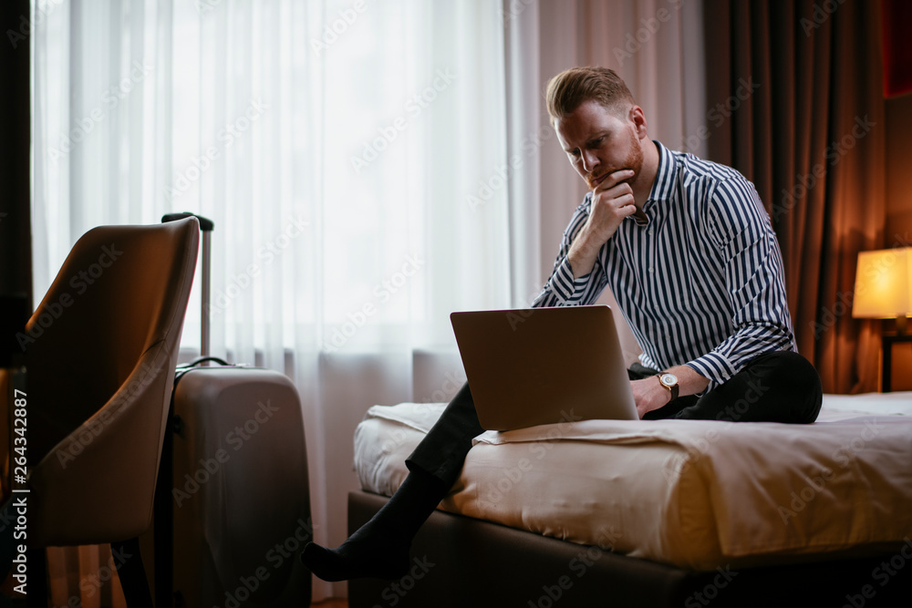 Man working on his laptop at the hotel. Executive manager working on his laptop at the hotel room. Businessman sitting on the bed working. Man working on his laptop at the hotel. Executive manager working on his laptop at the hotel room. Businessman sitting on the bed working.