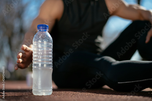 Thirsty athlete. Man reaching for a bottle of water. Guy trains outdoors.