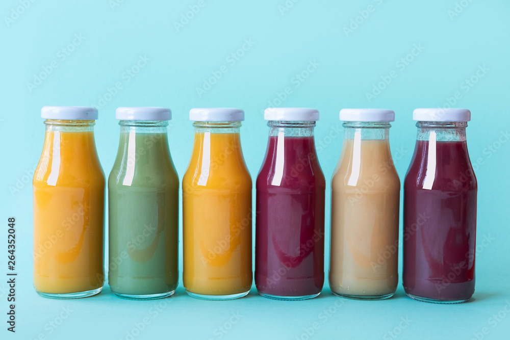 Raw vegetable and fruit juices in glass bottles on blue background Raw vegetable and fruit juices in glass bottles on blue background