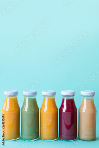 Raw vegetable and fruit juices in glass bottles on blue background. Copy space