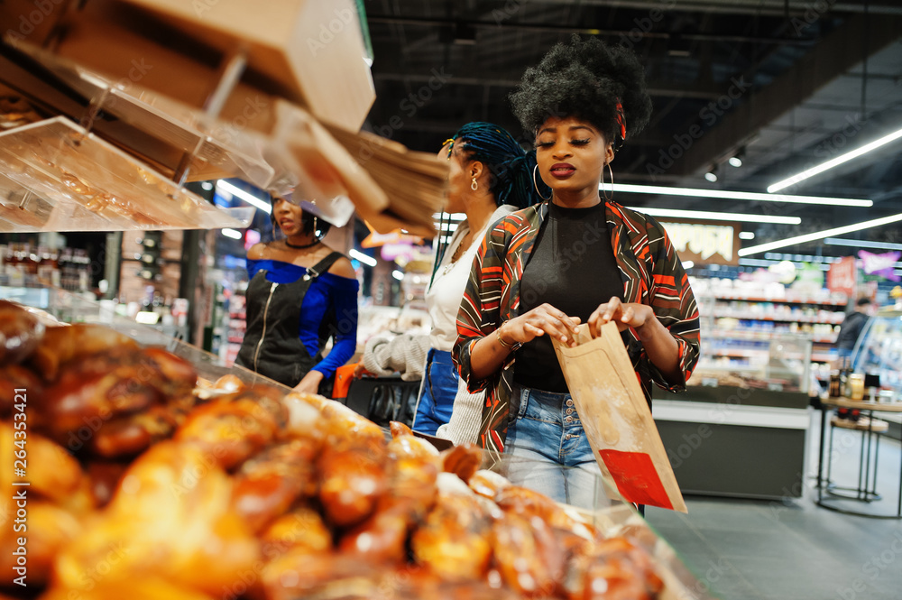 Group of african womans with shopping carts near baked products at a supermarket.