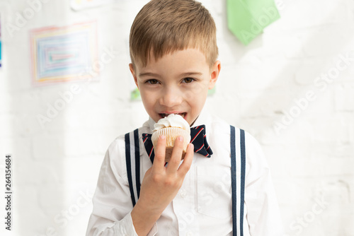 Schilderij op canvas adorable preteen boy in bow tie eating cupcake and looking at camera