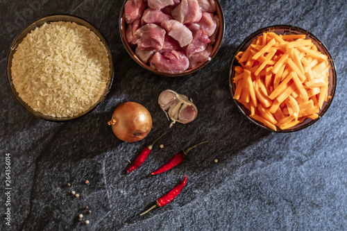 Ingredients for making pilaf, rice, meat, onions and carrots on a dark background
