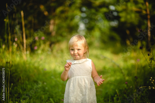 Beautiful little girl in white dress eating one small flower in