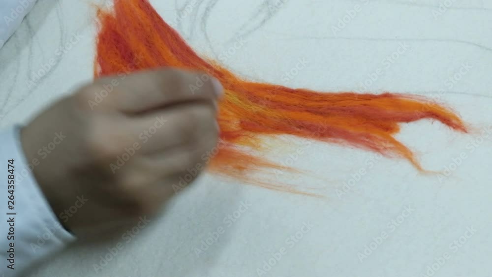 Close-up. A teenager in a white shirt pokes a needle over an orange dry felt. Making a picture of colored wool on a white fabric basis. Handicraft craft. Close-up. A teenager in a white shirt pokes a needle over an orange dry felt. Making a picture of colored wool on a white fabric basis. Handicraft craft.
