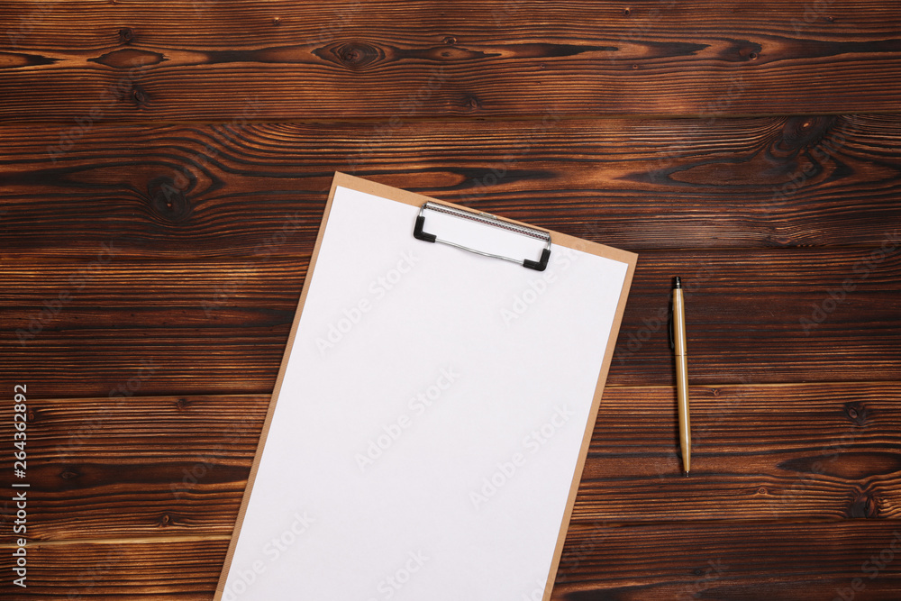Fototapeta premium Clipboard with white sheet on wood background. Top view.