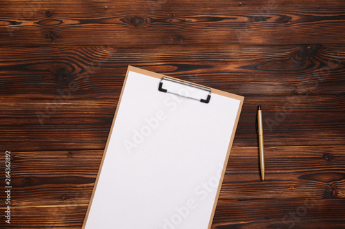 Clipboard with white sheet on wood background. Top view.