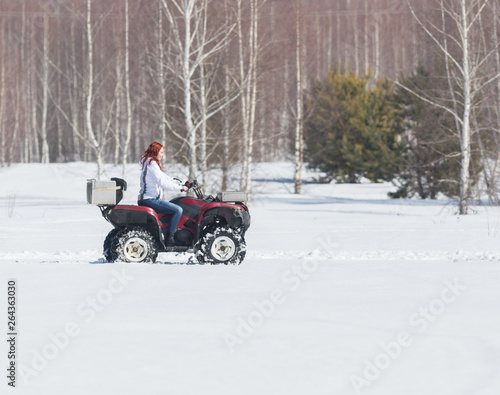 A winter forest. A woman with ginger hair riding big red snowmobile