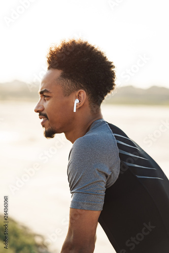 Handsome young african strong sports man listening music with earphones outdoors.