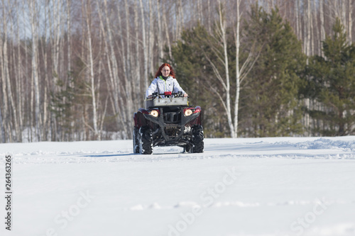 A winter forest. A woman with ginger hair riding red snowmobile