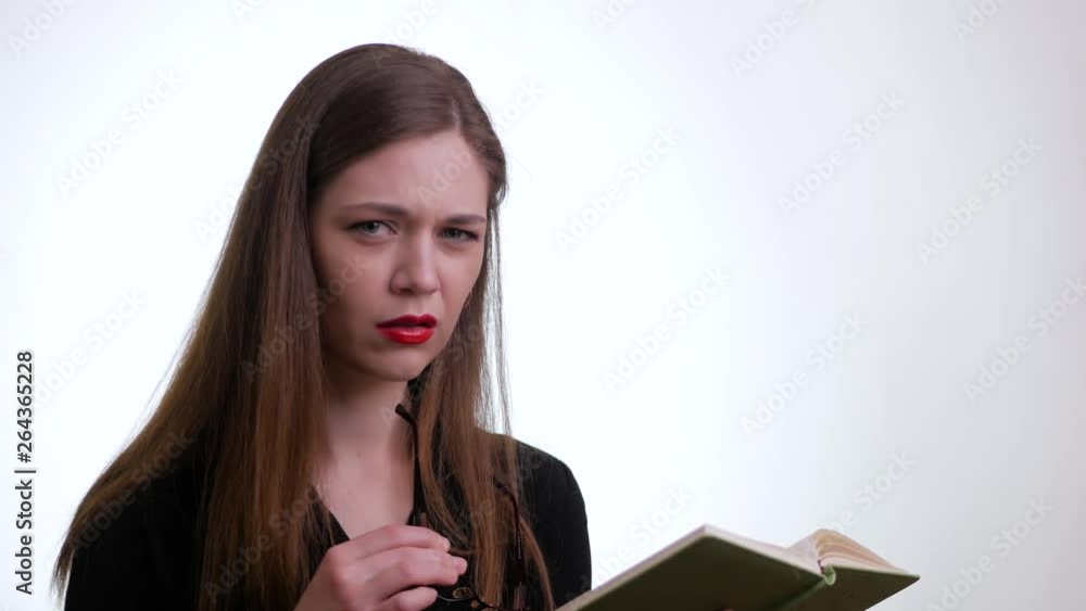 Young woman standing isolated over white background displeased because of reading book Young woman standing isolated over white background displeased because of reading book