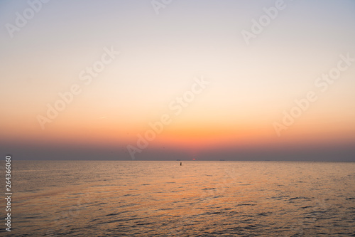 Lighthouse during a last minute of sunset with a big sun close to the horizon and clear sky