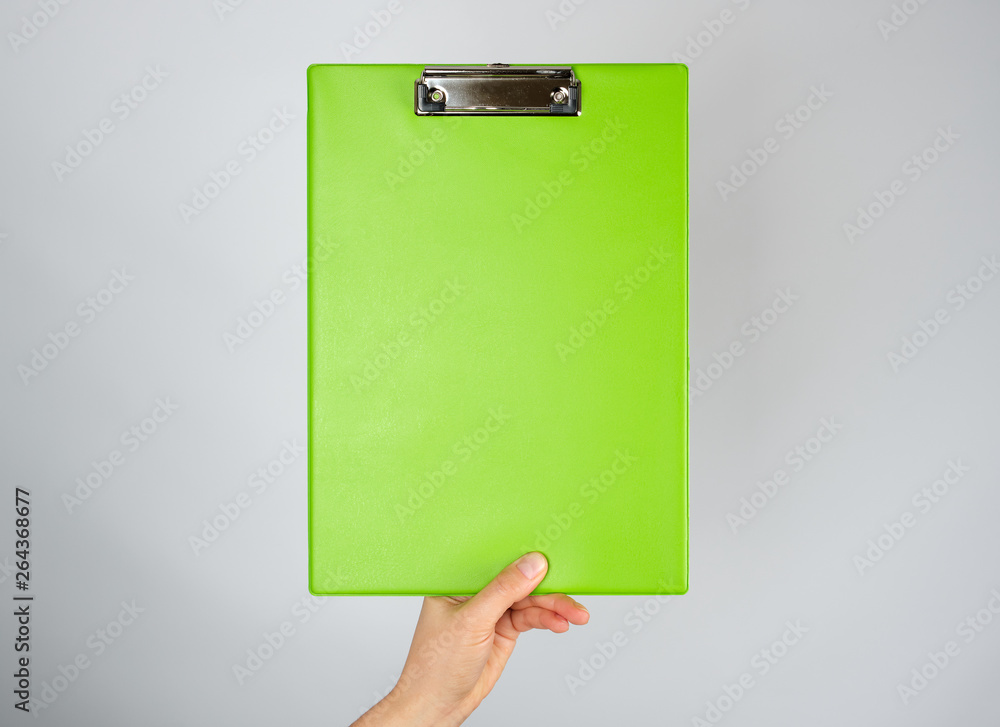 female hand holding a green clipboard for clamping papers female hand holding a green clipboard for clamping papers