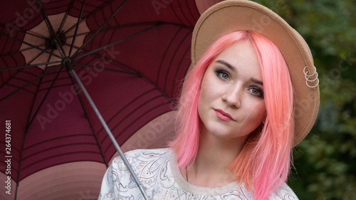 girl woman with pink hair and a hat looking at the camera and holding an umbrella. portrait.  horizontally