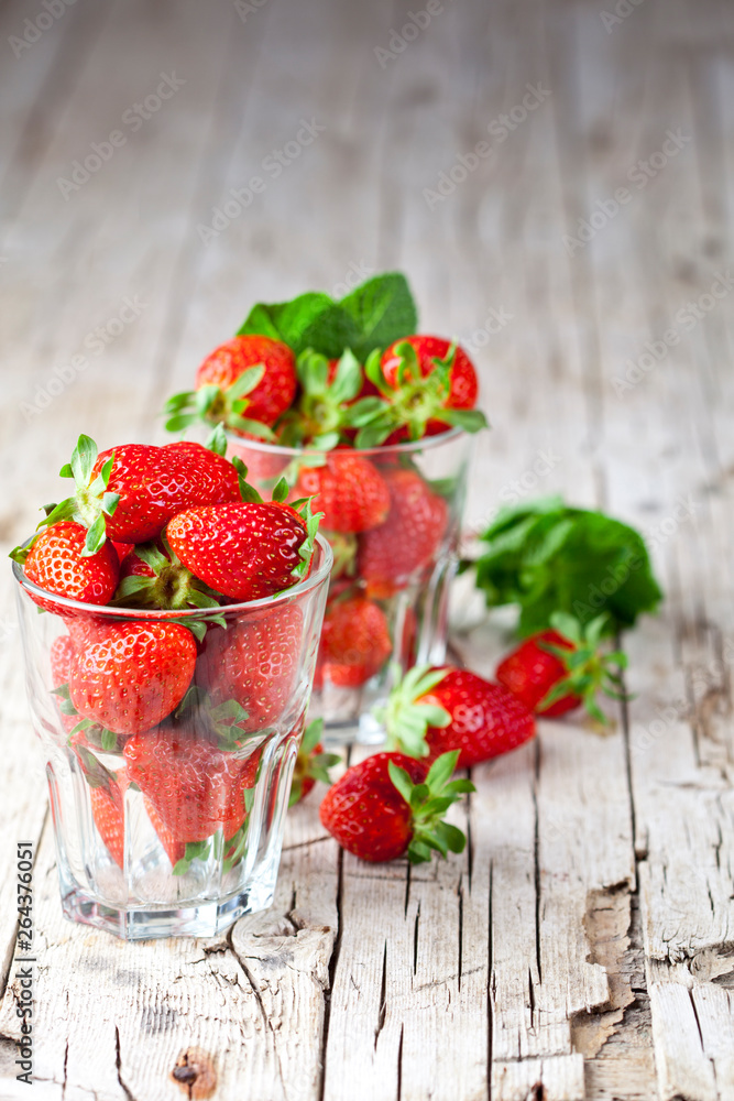 Organic red strawberries in two glasses and mint leaves on rustic wooden background. Organic red strawberries in two glasses and mint leaves on rustic wooden background.