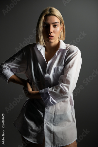 Fashion model. Young blond woman posing in studio wearing white shirt. Beautiful caucasian girl over gray background photo