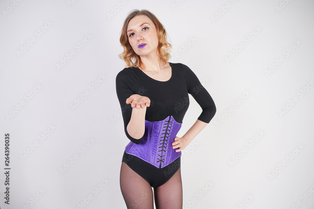 pretty fashionable blonde girl wearing black jumpsuit with mesh pantyhose and purple corset on white background pretty fashionable blonde girl wearing black jumpsuit with mesh pantyhose and purple corset on white background