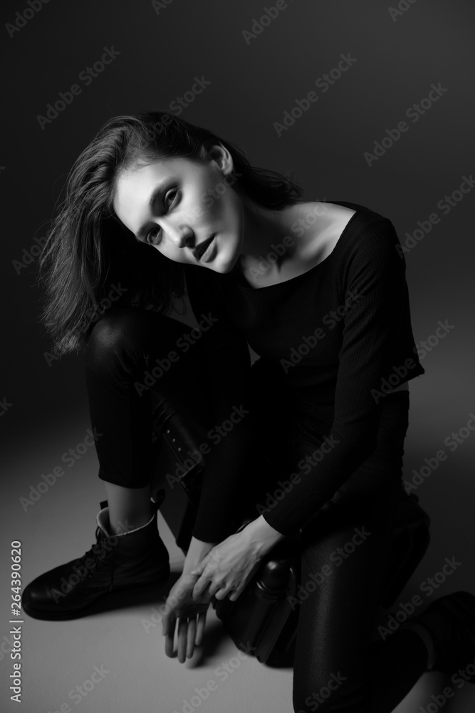 Fashion model. Young woman posing in studio wearing black with boots. Beautiful caucasian girl over gray background. Black and white Fashion model. Young woman posing in studio wearing black with boots. Beautiful caucasian girl over gray background. Black and white