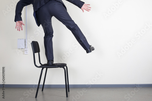 Businessman balancing while standing on an office chair against the wall with space for text.