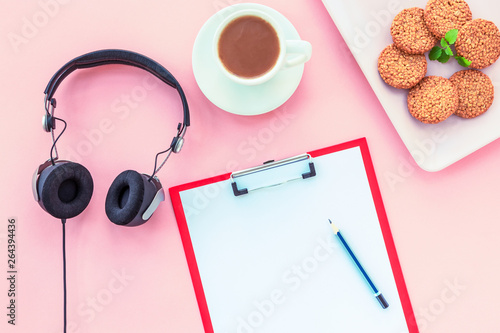 A cup of coffee, rice crackers, notebook with pencil and headphones on a pink background. Cosy workspace. Top view, flat lay.