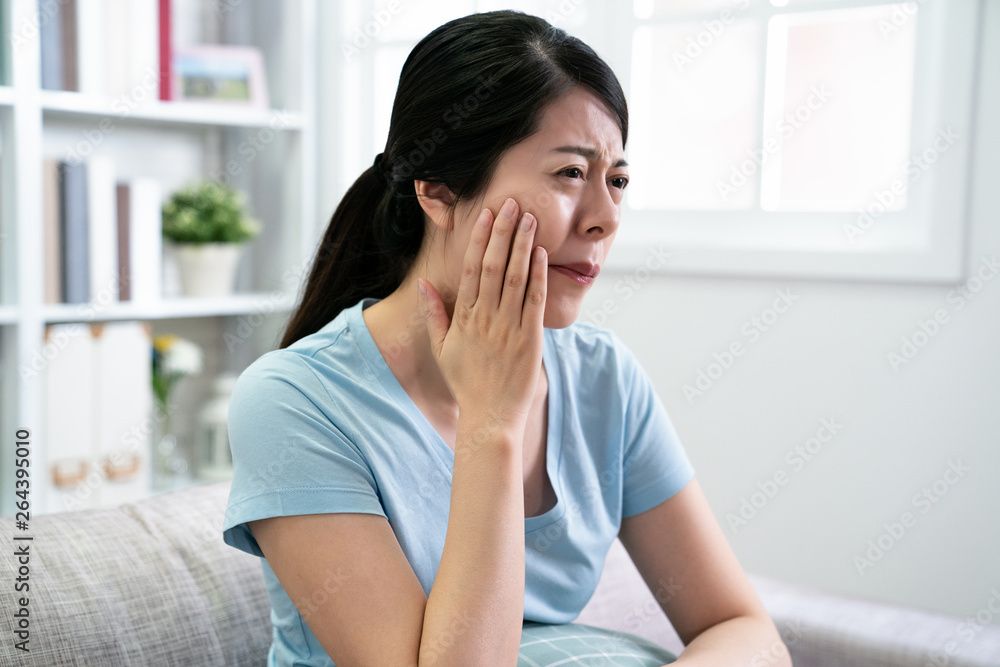 beautiful elegant asian woman has toothache sitting on couch with hurting uncomfortable face frowning. young chinese housewife at home having teeth painful problem. unhealthy concept illness female. beautiful elegant asian woman has toothache sitting on couch with hurting uncomfortable face frowning. young chinese housewife at home having teeth painful problem. unhealthy concept illness female.