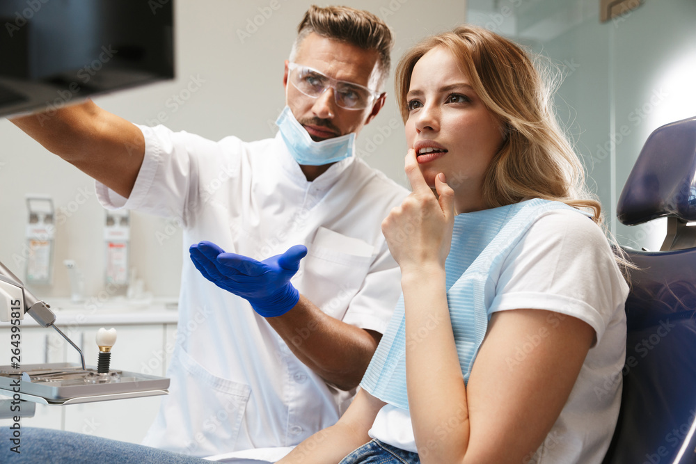 Fototapeta premium Photo of smiling woman sitting in medical chair at dental clinic while doctor fixing her teeth