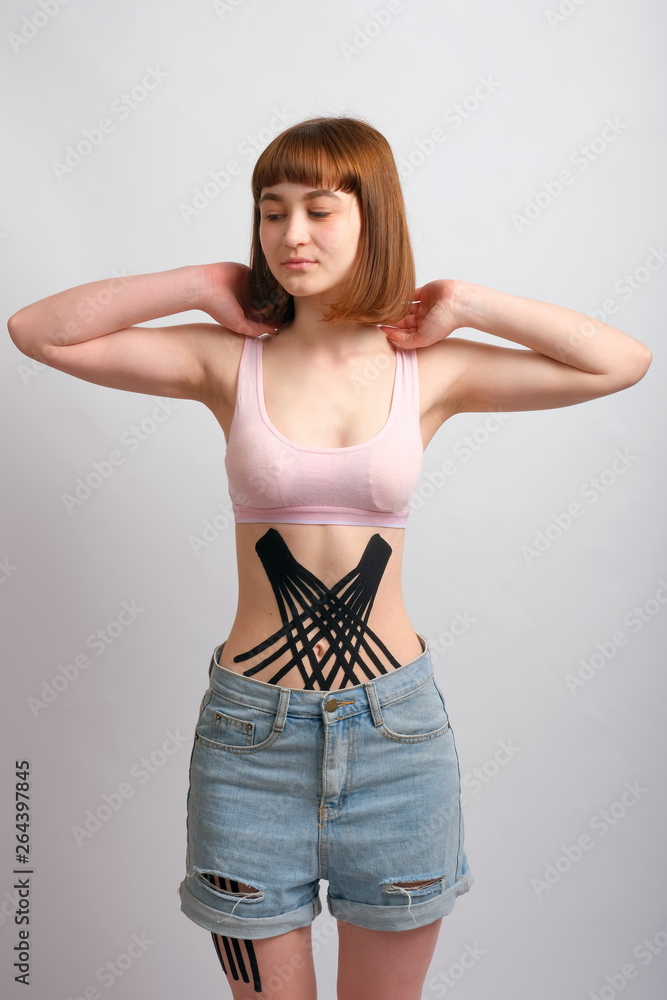 Crossed kinesio tape on the abdomen of young caucasian girl on white background.