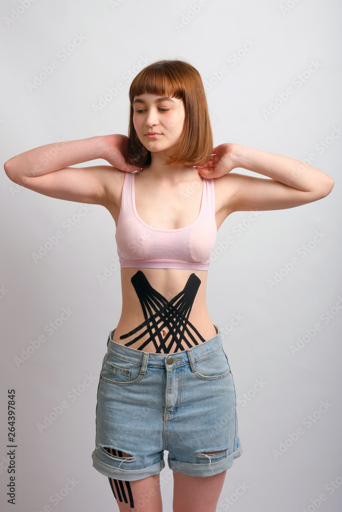 Crossed kinesio tape on the abdomen of young caucasian girl on white background. Crossed kinesio tape on the abdomen of young caucasian girl on white background.