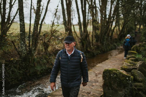 Man hiking in the Camino de Santiago way, crossing a stone bridge by the river.