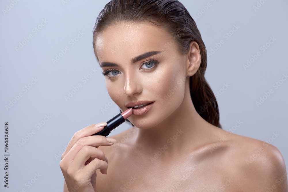 Obraz premium woman applying lipstick and looking into camera, girl with lipstick, pretty brunette applying lipstick, beautiful girl applying make-up
