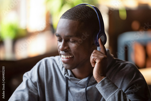 Serene african american guy wearing headphones listening favorite music