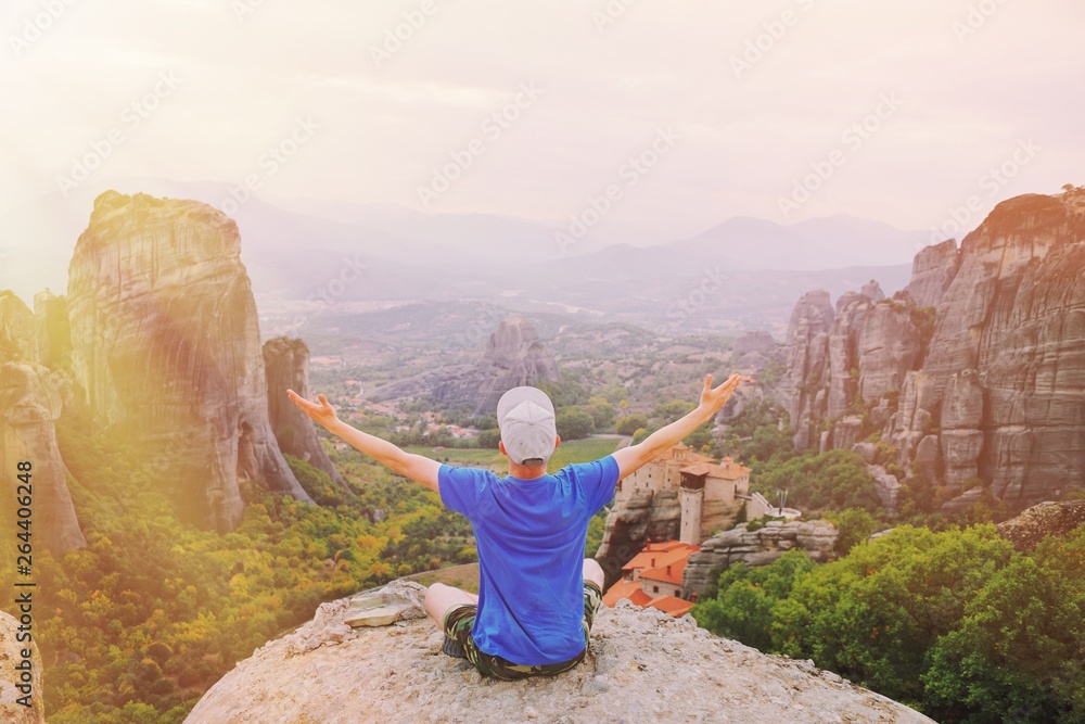 Man traveler praying at sunset mountain summit enjoying aerial epic view raised hands Travel lifestyle success relaxation. Emotional vacations, outdoor adventure freedom, harmony with nature concept.