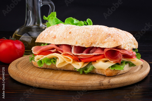 Ciabatta sandwich with lettuce , prosciutto and cheese on wooden board