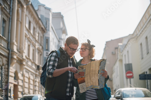 A young couple of tourists are looking for a road with a map in their hands in the city.