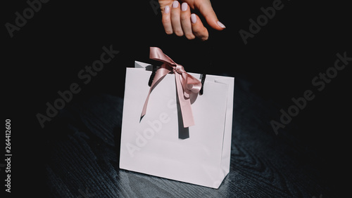 Hand holding paper bag on white background. Women with beautiful manicure. White paper beg with pink bow.