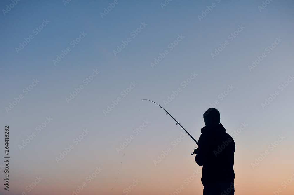 Silhouette of a fisherman at sunset against the sky